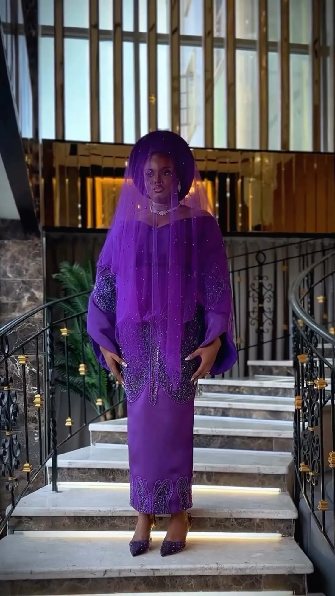 Bride in purple lace and a veiled gele on a staircase