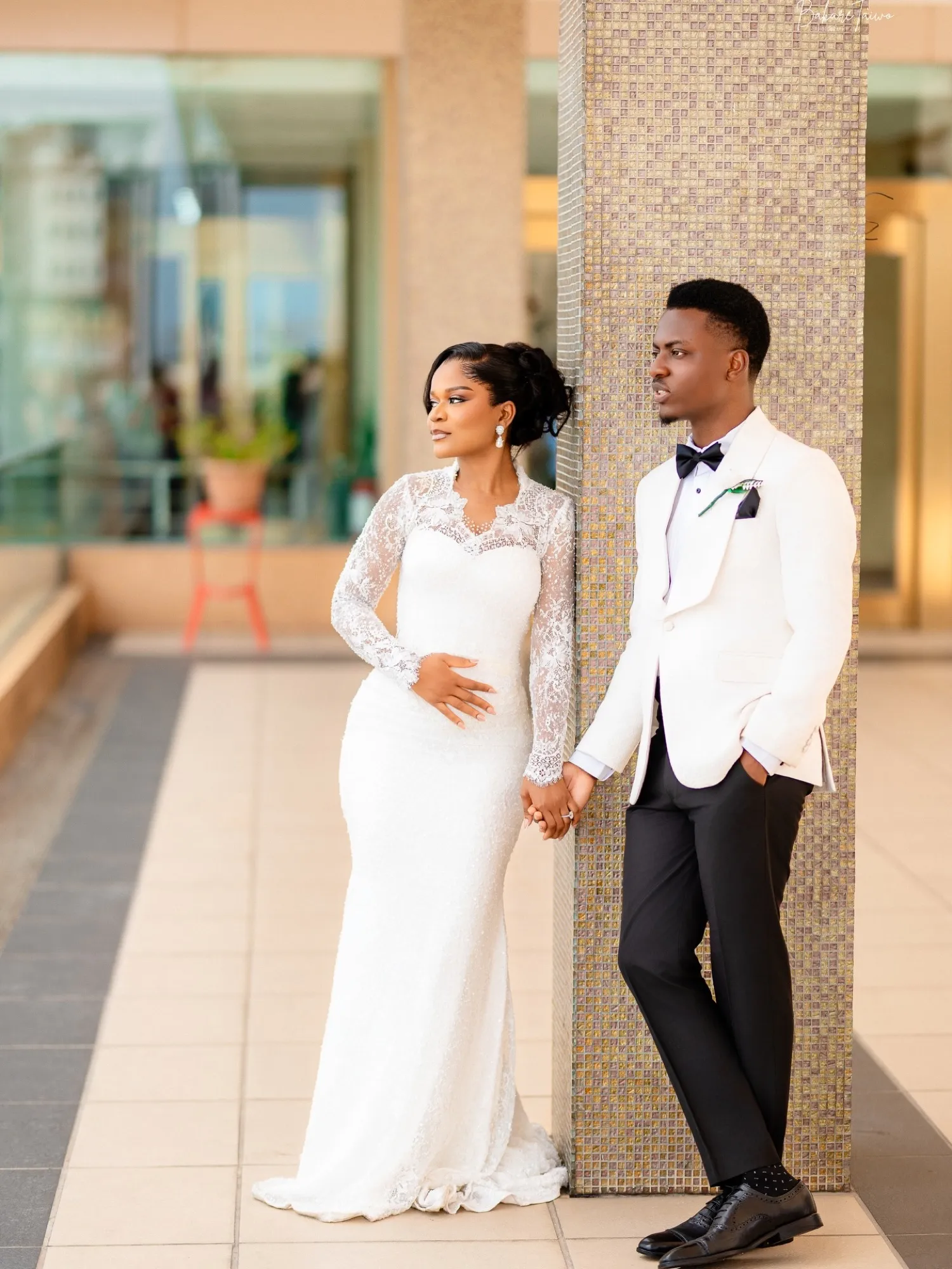 A bride and groom in white on a sunlit courtyard