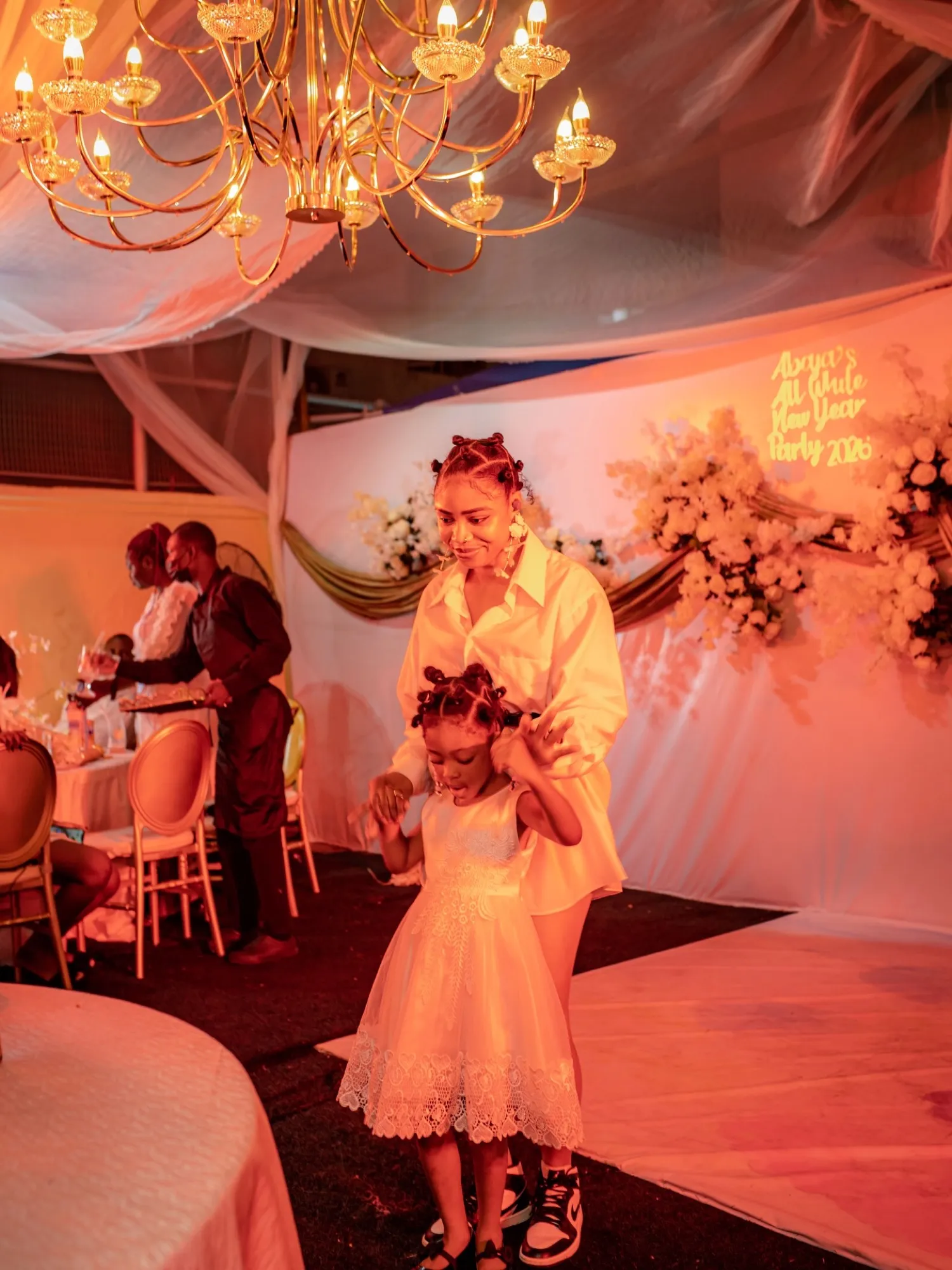 A little girl in a white dress under a gold chandelier