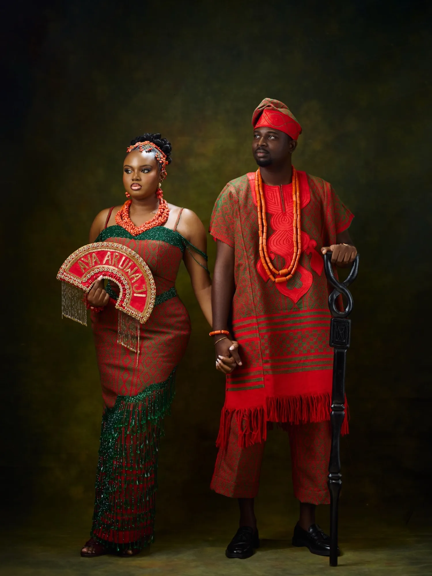 The couple in red and coral traditional attire with a beaded fan