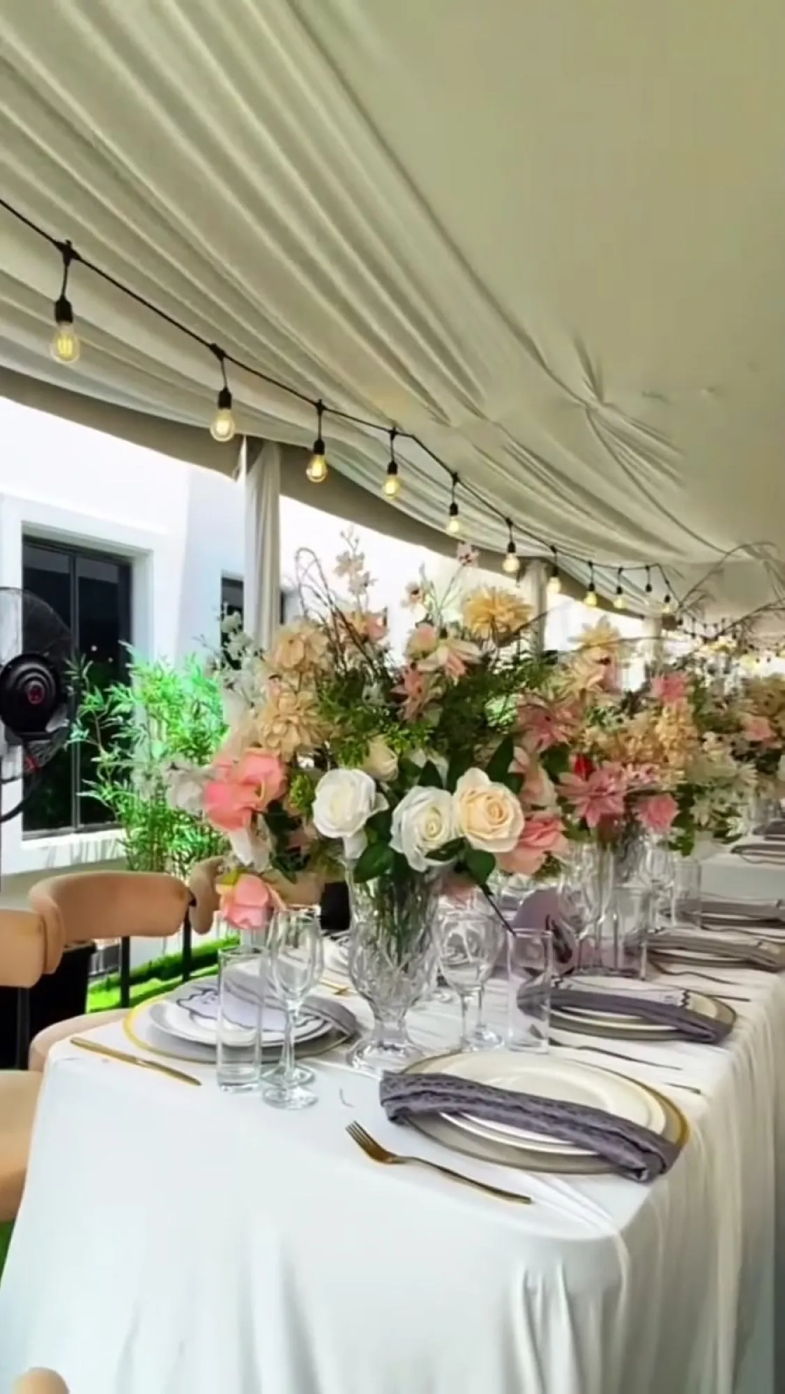 A long table under a white canopy, blush florals, gold-rimmed plates and a menu card at every seat.