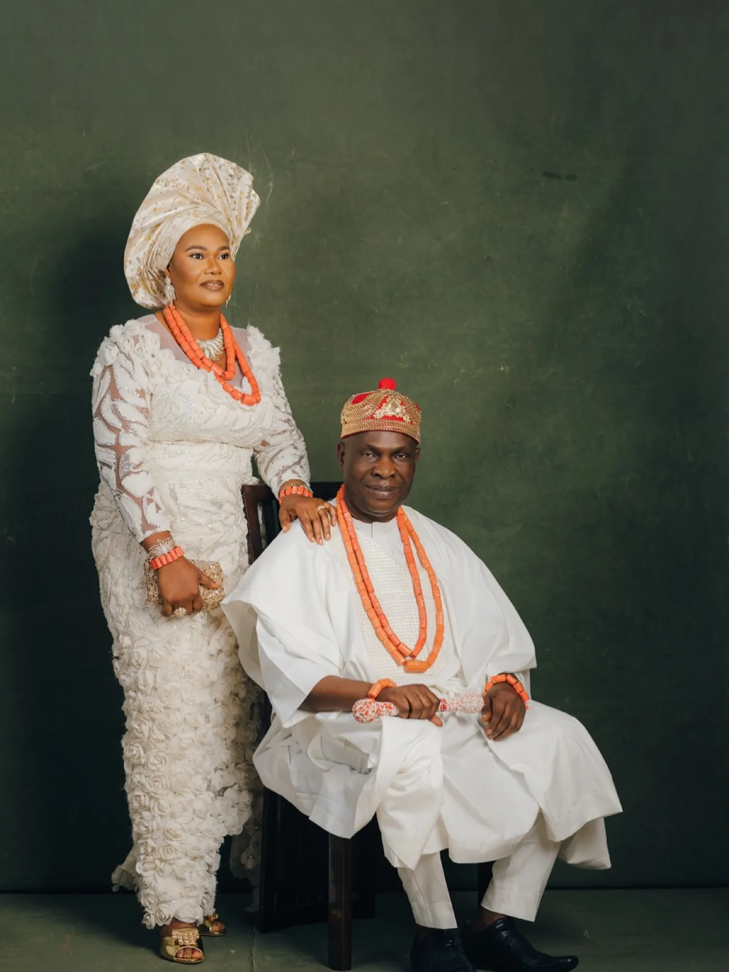 HRM seated in white with coral beads beside his queen in white lace and gele