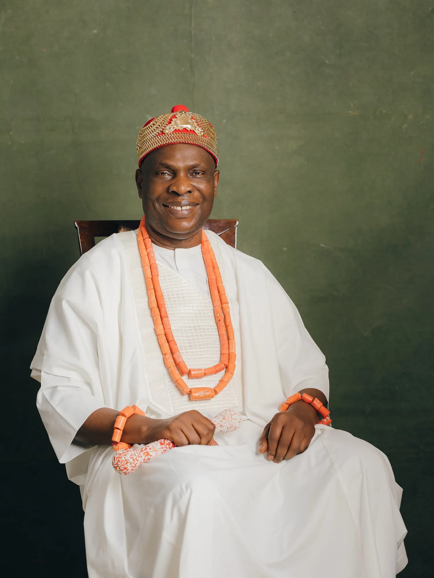 HRM smiling, seated in white with layered coral beads