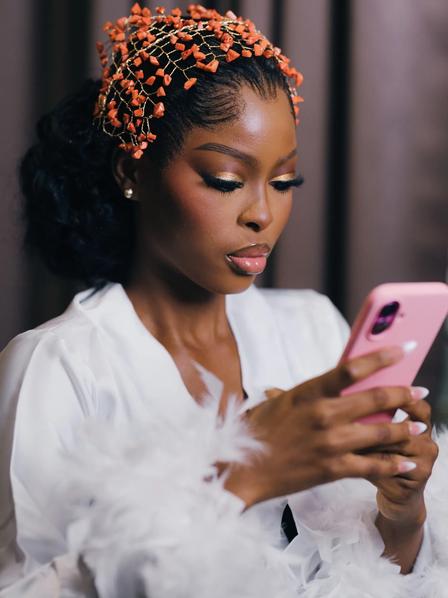 Feyi in coral beads checking her phone during glam