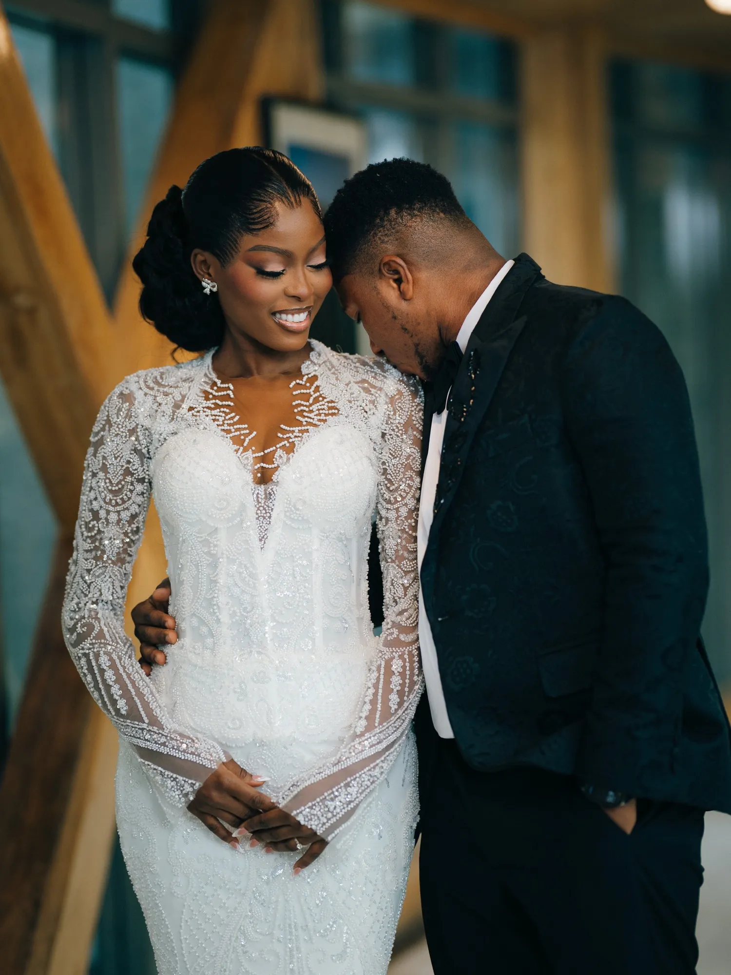 The couple leaning in close, bride in long-sleeved lace
