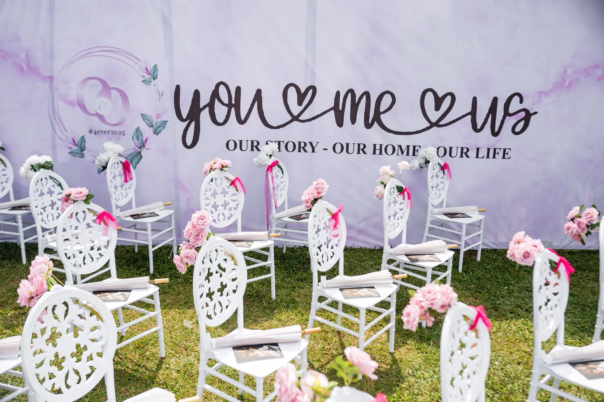 “you ♡ me ♡ us” backdrop behind rows of white chairs