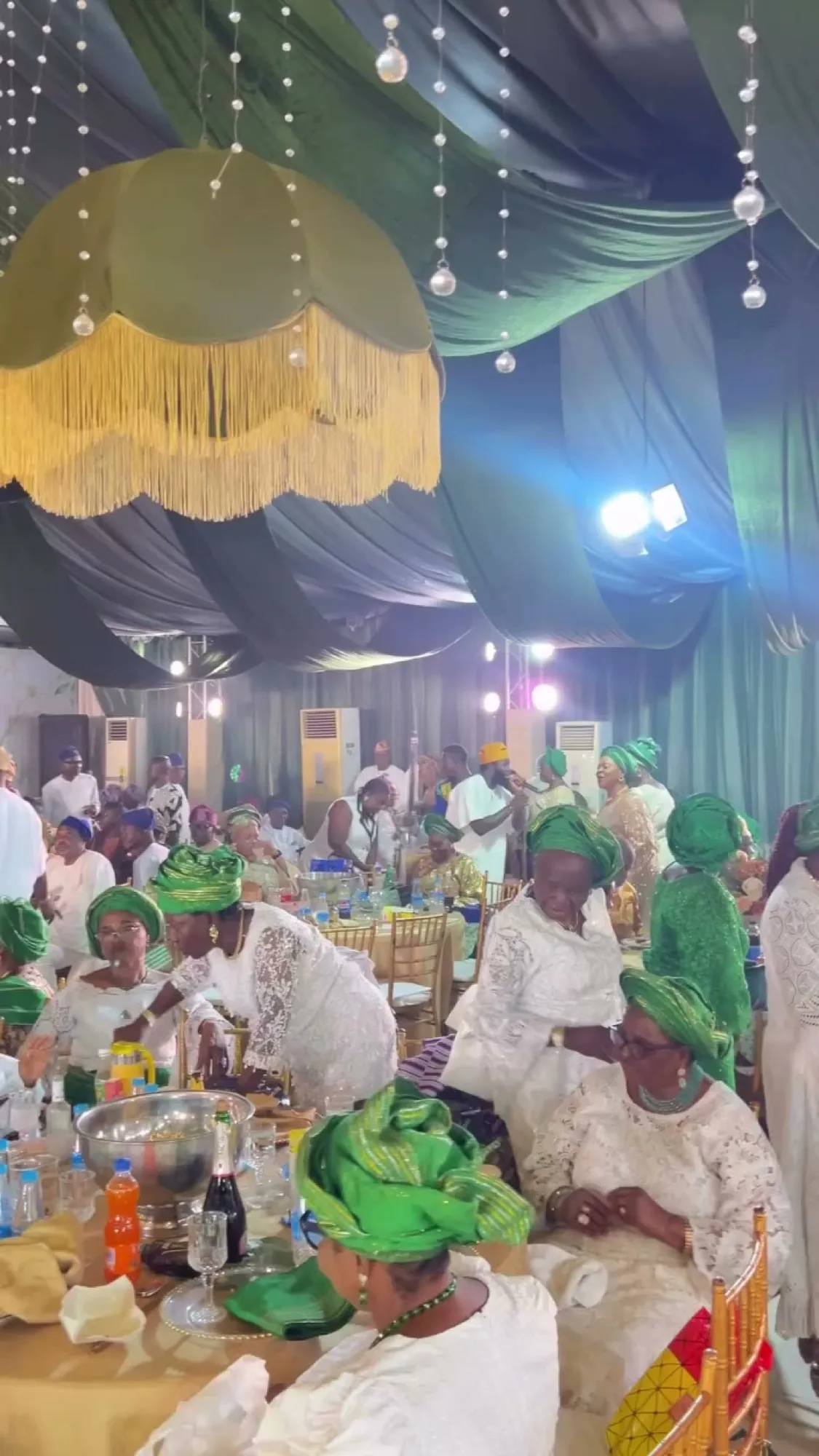 Guests in green and gold under fringed lampshade chandeliers